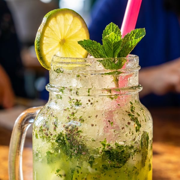 Refreshing mojito in a mason jar with lime and mint, with people dining in the background.