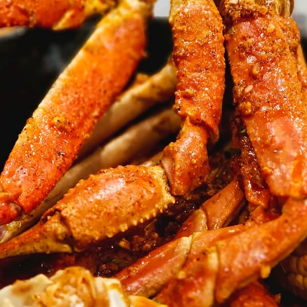 Close-up of seasoned crab legs and corn on the cob in a dark bowl.