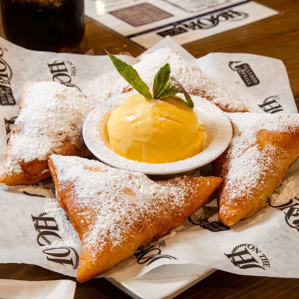 Golden-fried beignets dusted with powdered sugar surround a scoop of ice cream with mint.